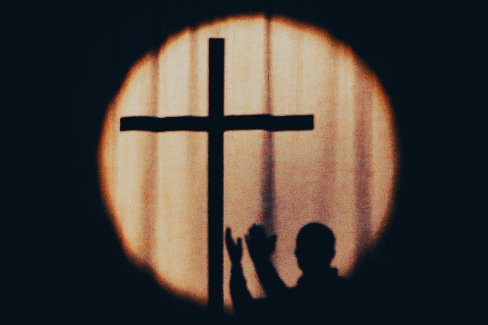 A silhouette with hands raised in prayer before a wooden cross