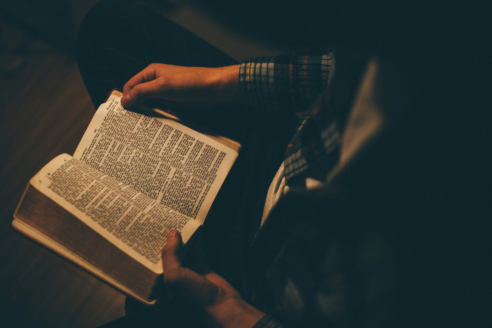 Hands holding an open Bible under warm lamp light